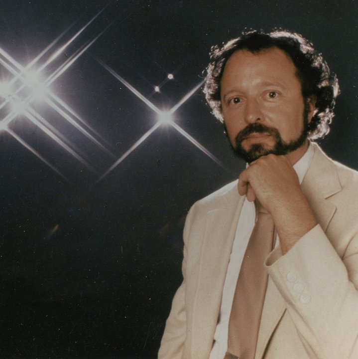 Steven Forrest in a light-colored suit against a starry studio background in the 1990s